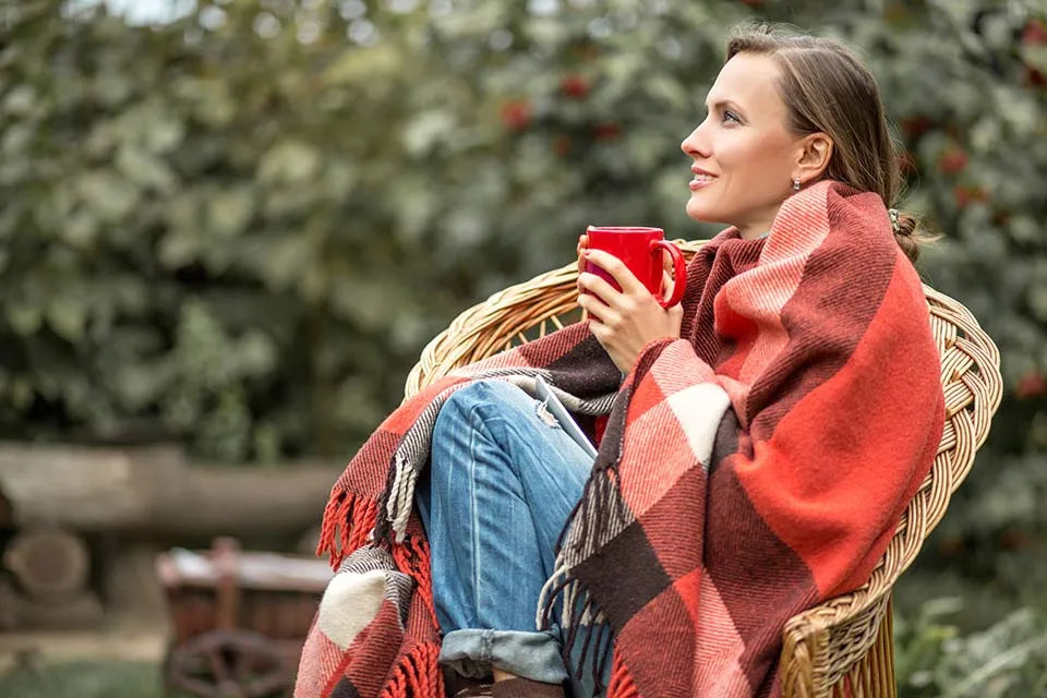 Vrouw met een mok in een tuinstoel, gewikkeld in een roodgeruite deken.
