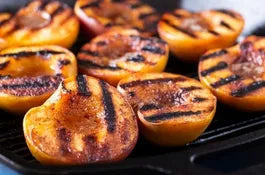 Gehalveerde perziken met donkere grillstrepen op een barbecuerooster.
