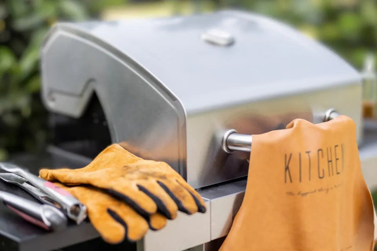 Gasbarbecue met tuinhandschoenen, barbecuetang en een leren schort.