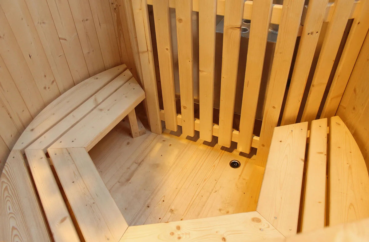 Binnenkant van een lege houten hottub met zitbanken langs de wand en een afgeschermd metalen onderdeel.