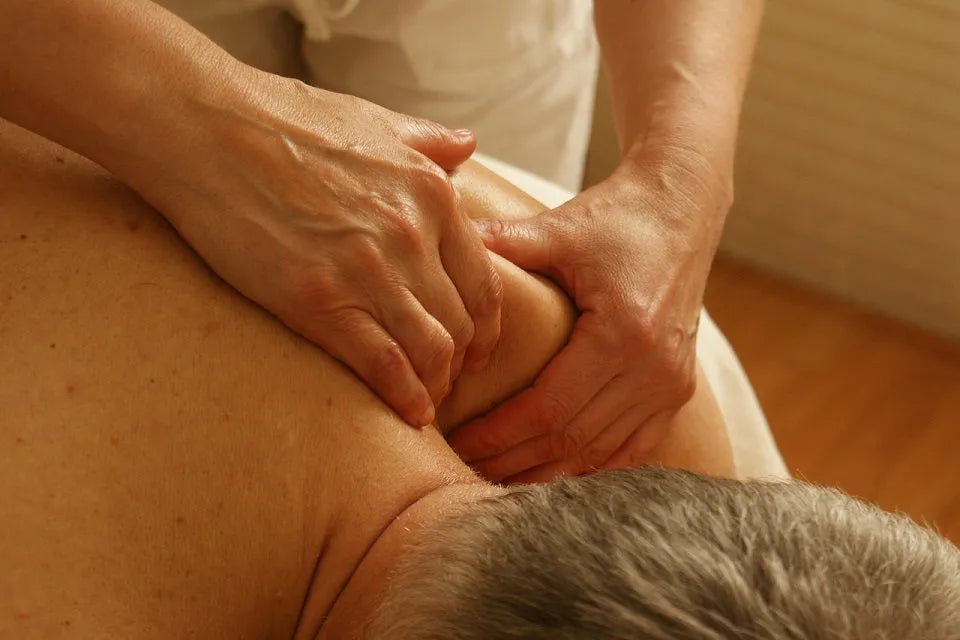 Handen masseren de nek en schouders van een liggende persoon.