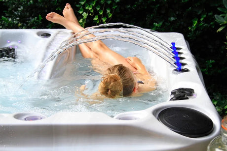 Persoon ligt achterover in een bruisend wit spabad onder boogvormige waterstralen.