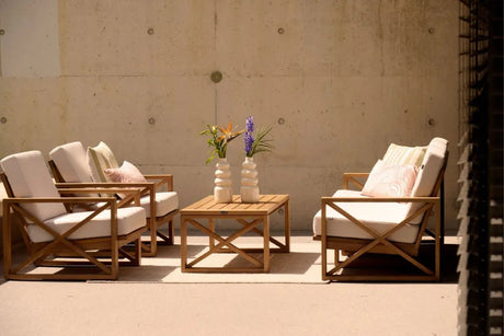 Houten loungebank en stoelen met lichte kussens rond lage tafels op een terras.