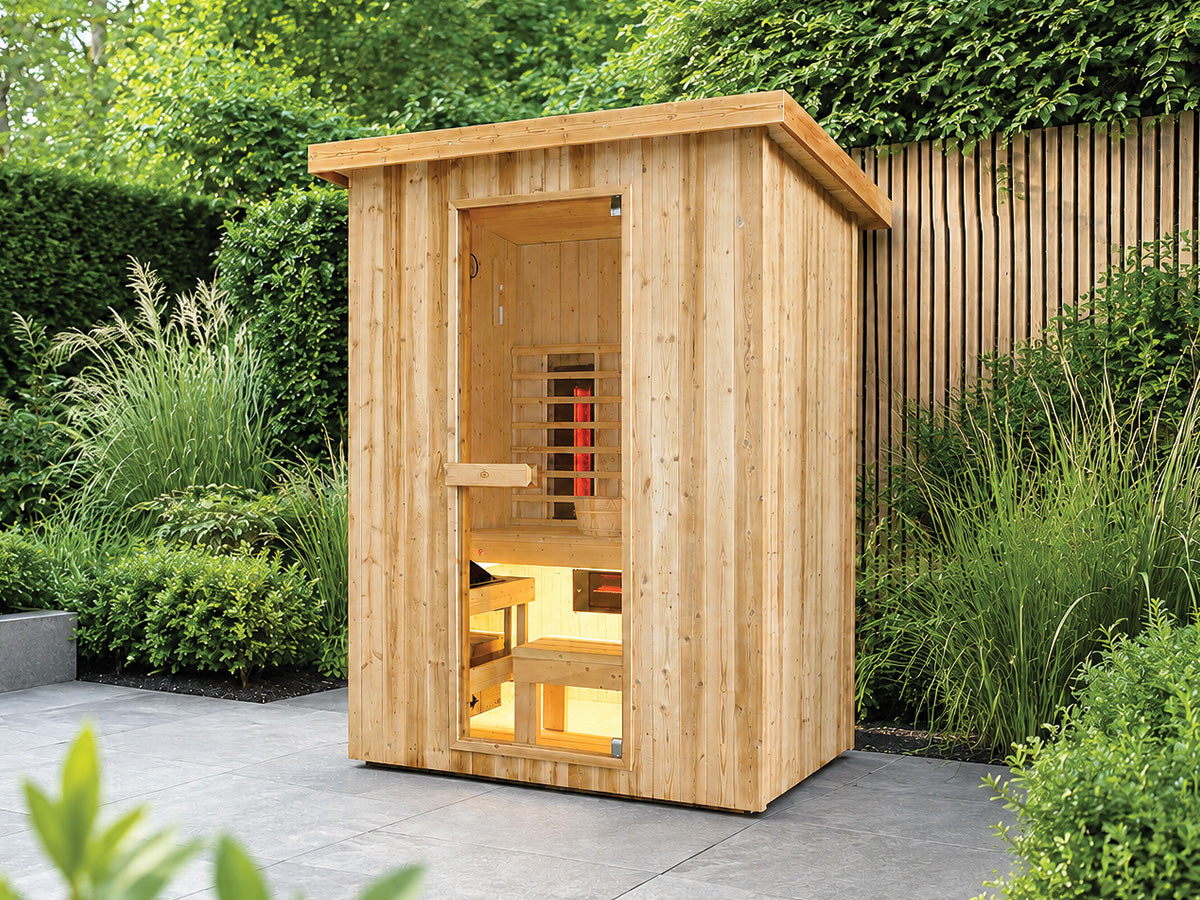 Fonteyn Retreat 150 houten buitensauna met glazen deur en verlicht interieur op een terras in een groene tuin.