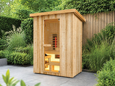 Fonteyn Retreat 150 houten buitensauna met glazen deur en verlicht interieur op een terras in een groene tuin.