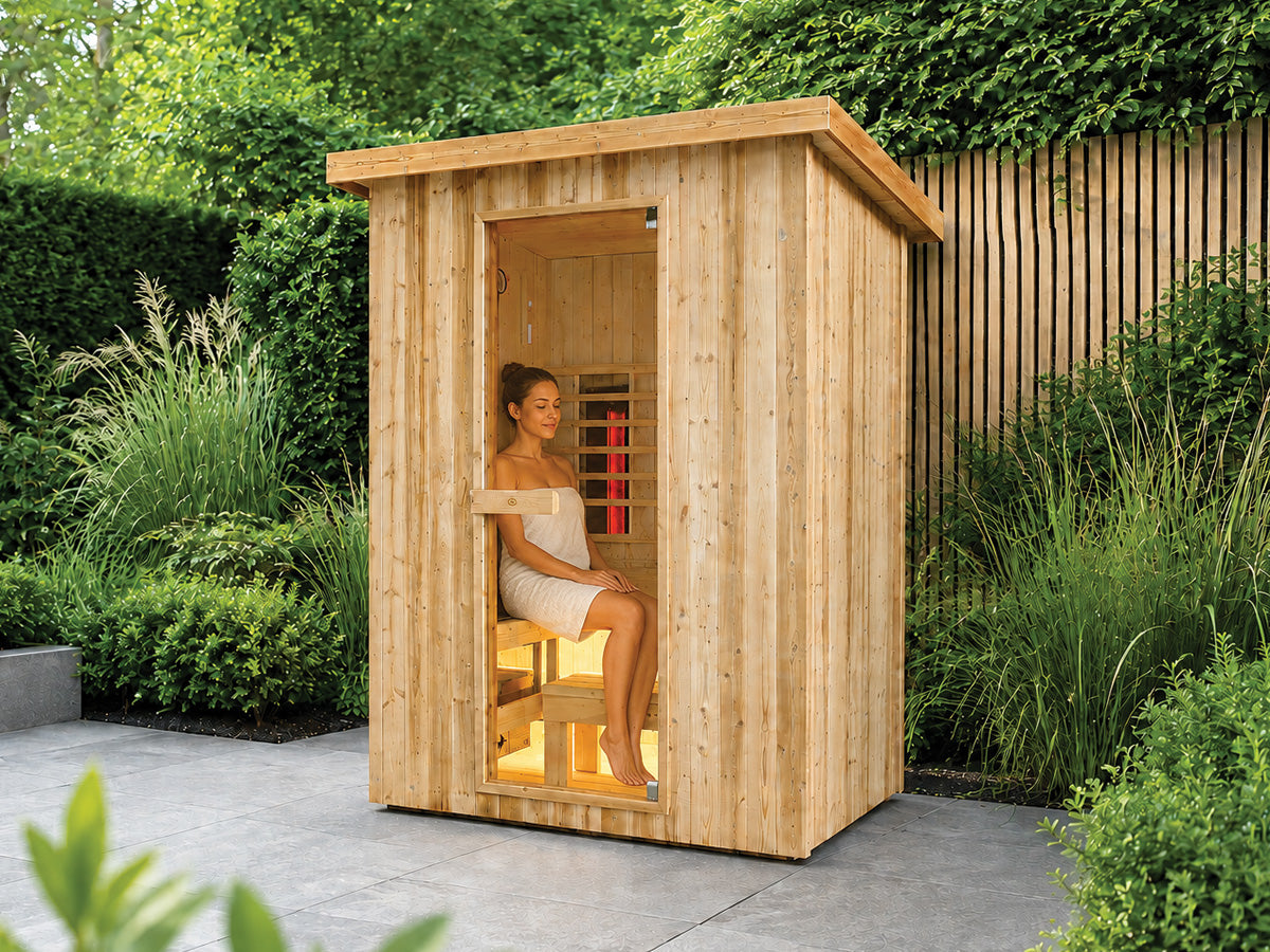 Fonteyn Retreat 150 buitensauna met een persoon op de bank achter de glazen deur, op een terras in de tuin.