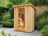 Fonteyn Retreat 150 buitensauna met een persoon op de bank achter de glazen deur, op een terras in de tuin.